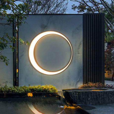 The ring lit on a stone wall above a still pool and a planted edge at dusk