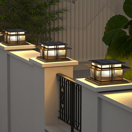 Two caps lit on rendered pillars above a slatted fence at dusk