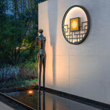 The light on a tall white wall beside a bronze figure above a dark pool