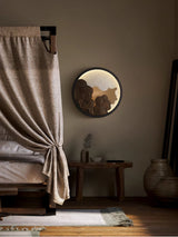 Sconce lit beside a long curtain above a bench and a tall floor vase