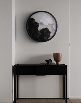 Sconce lit above a narrow black console holding two pale stone bowls