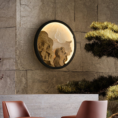 Sconce lit on a stone wall above two chairs with a clipped plant beside