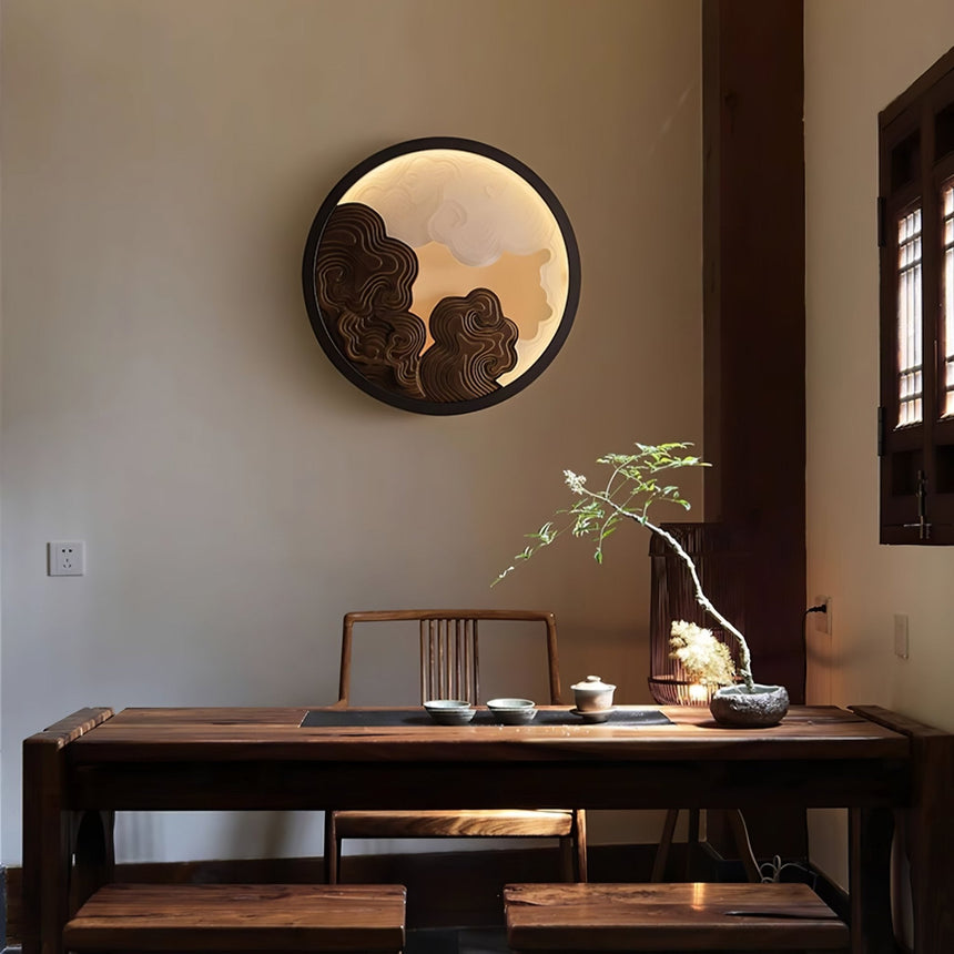 Sconce lit above a dark tea table with a small plant and a wood chair