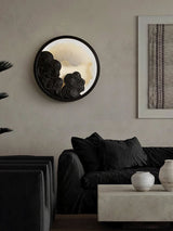 Sconce lit beside a framed textile above a dark sofa with cushions