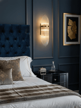 The sconce lit beside a navy tufted headboard and a framed gold artwork