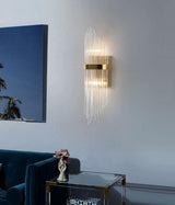 The sconce lit on a pale wall above a blue velvet sofa and a glass side table