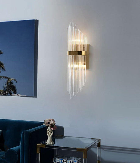 The sconce lit on a pale wall above a blue velvet sofa and a glass side table