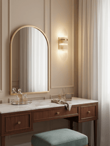 The sconce beside an arched mirror above a wood dressing table and a stool