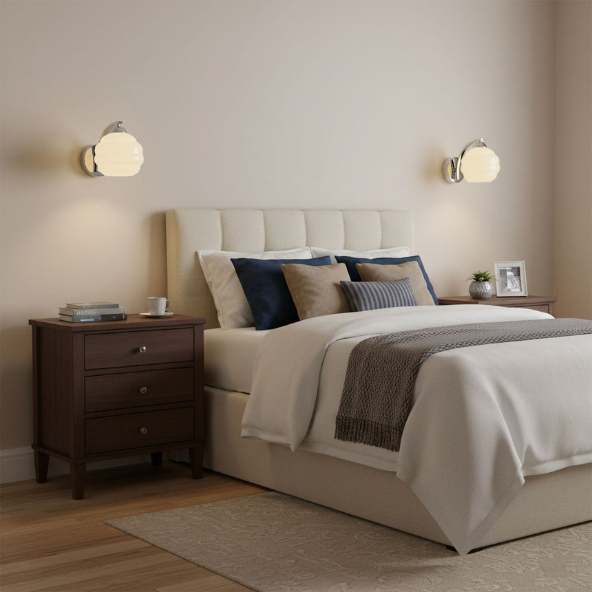 Two sconces lit above wood nightstands in a bedroom with a tufted headboard