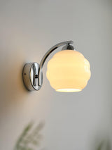 The chrome sconce lit on a gray wall, the ribs of the globe glowing warm