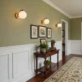 Sconces lit on a green wall above white paneling and a console table