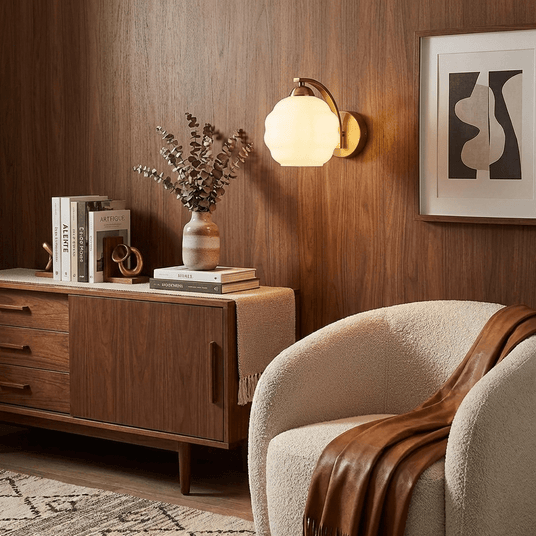 The gold sconce lit on a wood paneled wall above a sideboard and an armchair