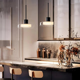 Two glass disc pendants lit above a dark marble counter with wooden chairs