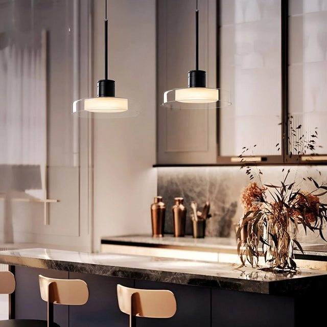 Two glass disc pendants lit above a dark marble counter with wooden chairs
