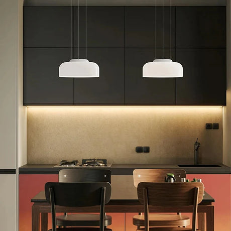 Two white glass pendants lit above a dining table in a dark room