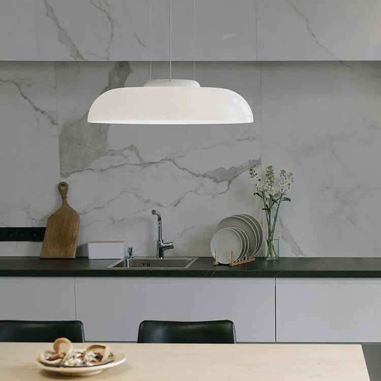 Low white glass shade hung in front of a marble kitchen backsplash