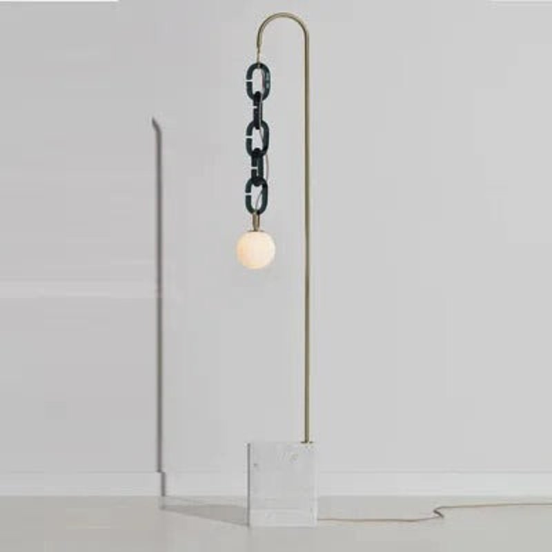 A brass rod hooking over to hang a dark glass chain and a white globe above a stone base