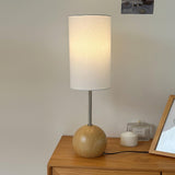Natural wood globe table lamp lit on a wooden surface beside candles