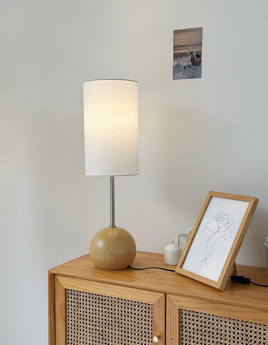 Natural wood globe table lamp lit on a sideboard beside a candle