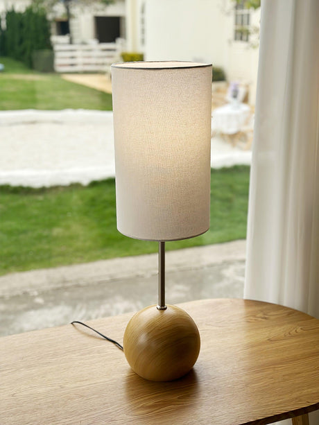 Natural wood globe table lamp on a table in front of a garden window