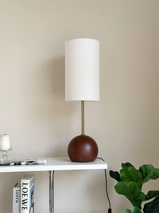 Walnut globe table lamp lit on a console beside books and a candle