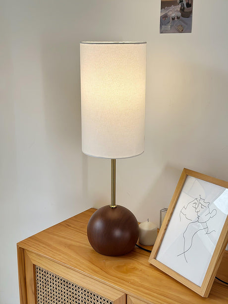 Walnut globe table lamp lit on a sideboard in front of a framed drawing