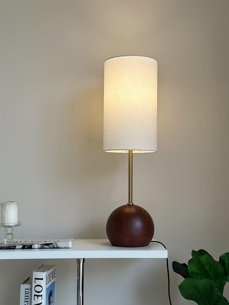 Walnut globe table lamp lit on a console beside a green plant