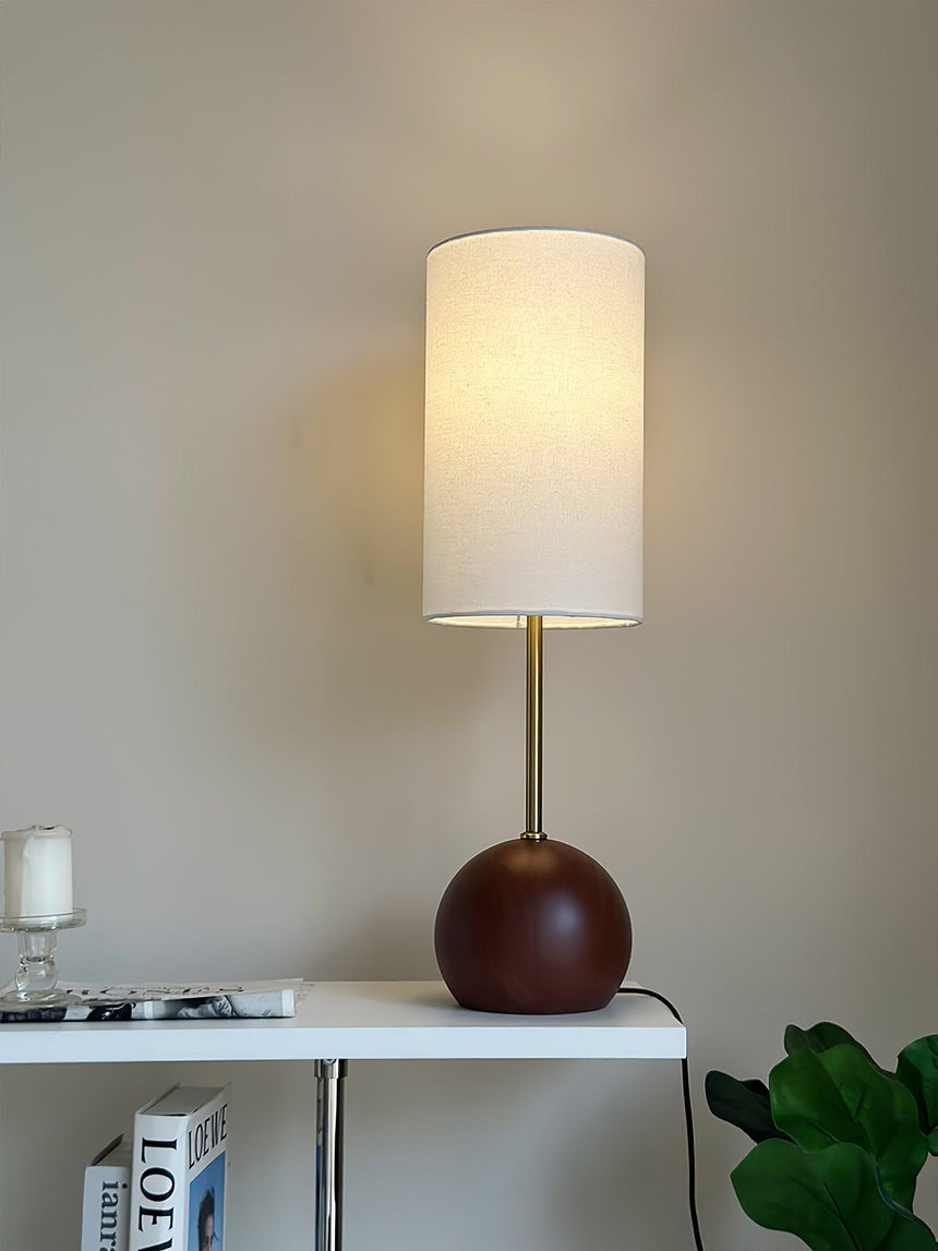 Walnut globe table lamp lit on a console beside a green plant