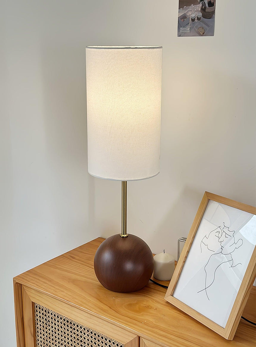 Walnut globe table lamp lit on a sideboard beside a framed picture