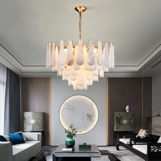 The lit chandelier in a living room with a sofa, a round mirror and artwork
