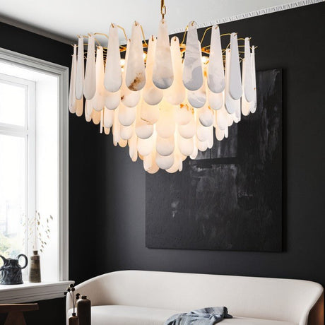 The lit chandelier above a white sofa beside a window and a dark canvas
