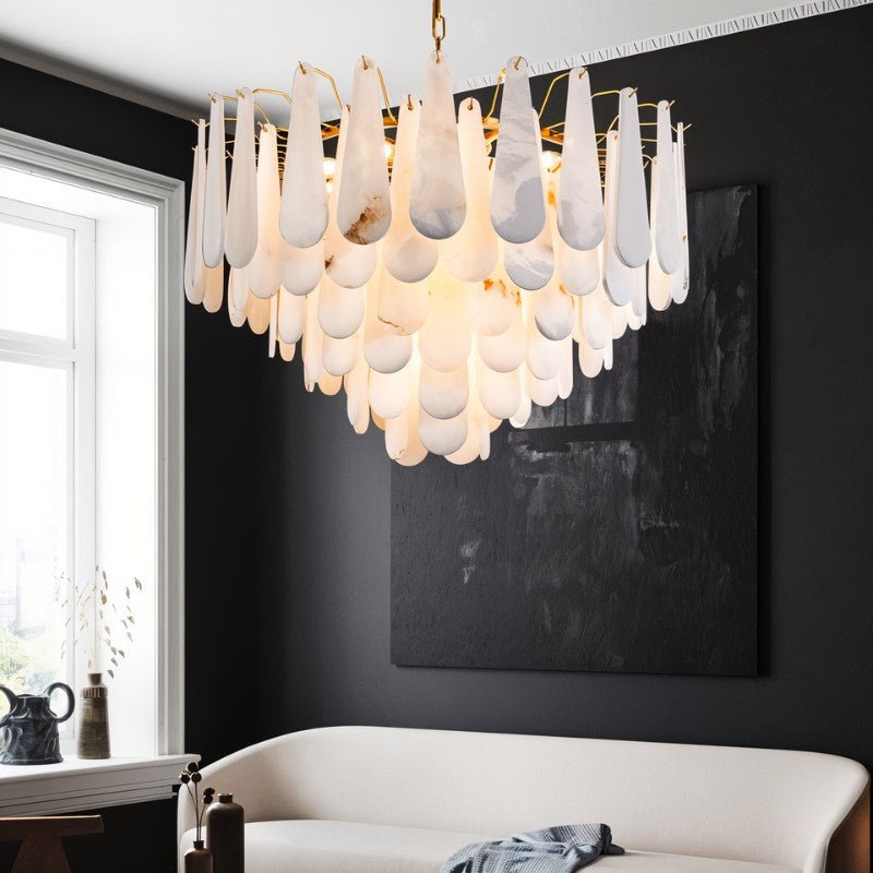 The lit chandelier above a white sofa beside a window and a dark canvas