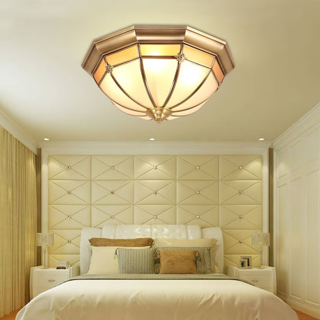Faceted brass dome ceiling light above a bed with a padded headboard