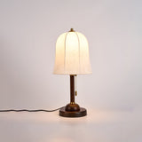 Gold and white table lamp lit and seen at an angle on a pale ground