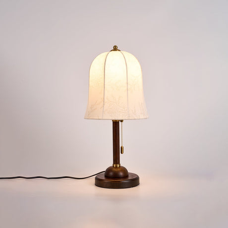 Gold and white table lamp lit and seen at an angle on a pale ground