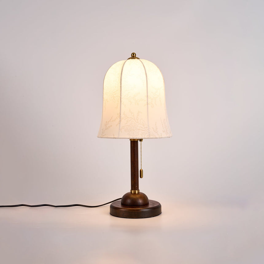 Gold and white table lamp lit and seen at an angle on a pale ground