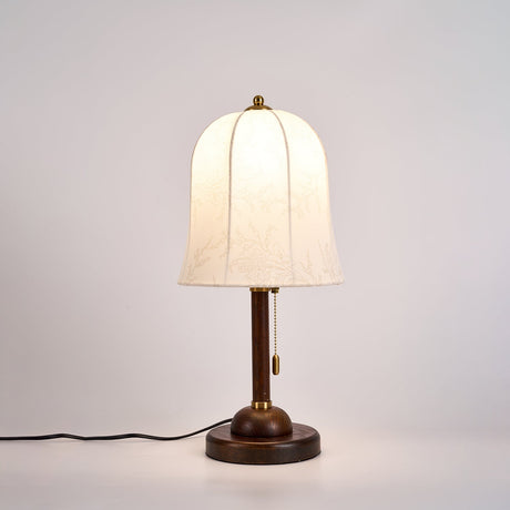 Gold and white table lamp lit from the front, the bell shade glowing