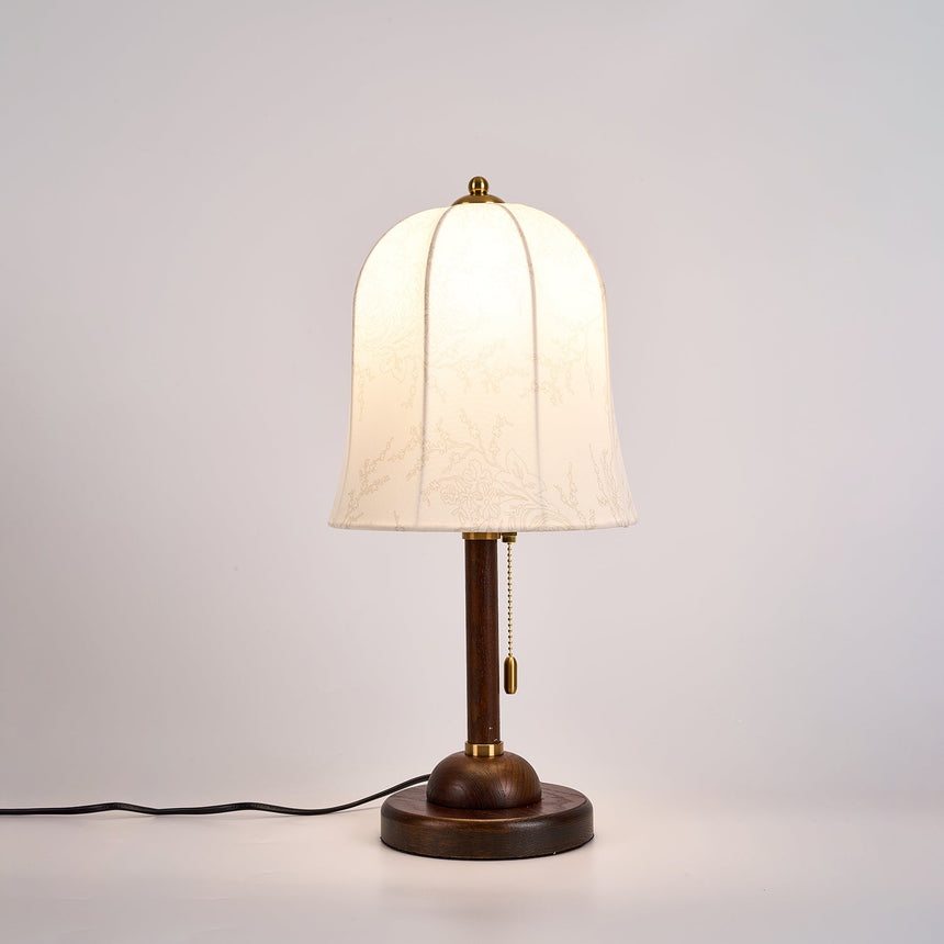 Gold and white table lamp lit from the front, the bell shade glowing
