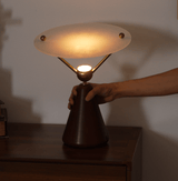 A hand lifting the gold and white table lamp by its wood cone base