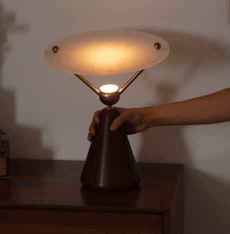 A hand lifting the gold and white table lamp by its wood cone base