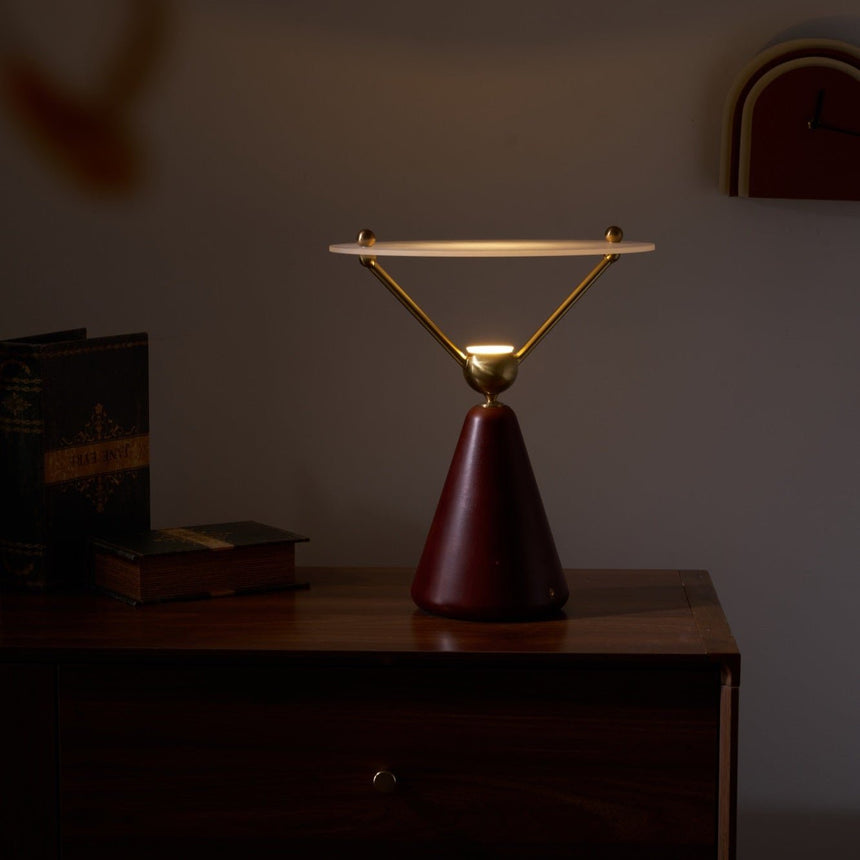 Gold and white table lamp lit on a wooden chest in a dim room