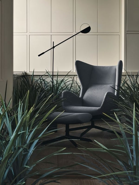 The lit lamp reaching over a dark armchair in a corner planted with tall grasses