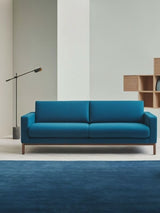 The lit lamp reaching over a blue sofa with cushions on a deep blue rug