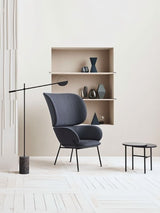 The lit lamp reaching over a gray chair beside open shelving with vases and books