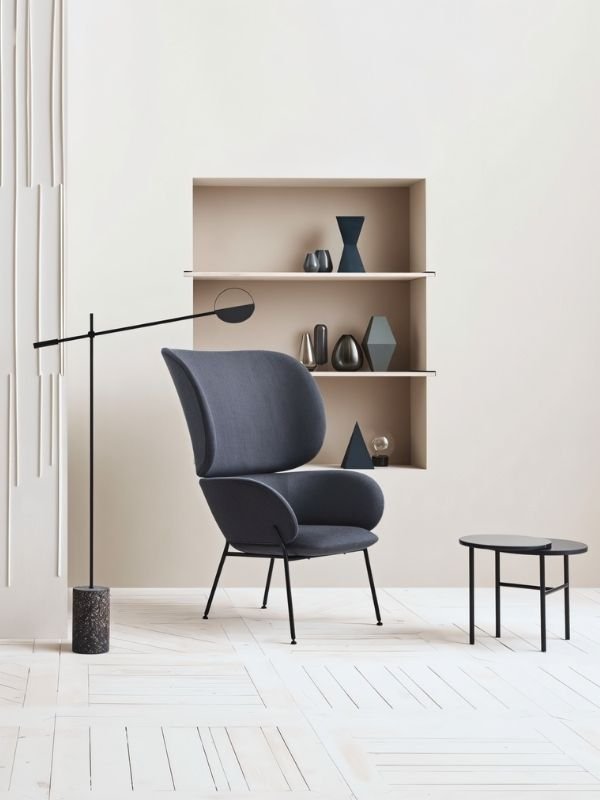 The lit lamp reaching over a gray chair beside open shelving with vases and books