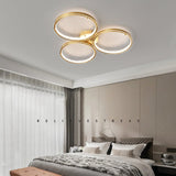 Three ring gold ceiling light above a bed with a dark throw