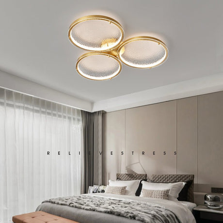 Three ring gold ceiling light above a bed with a dark throw