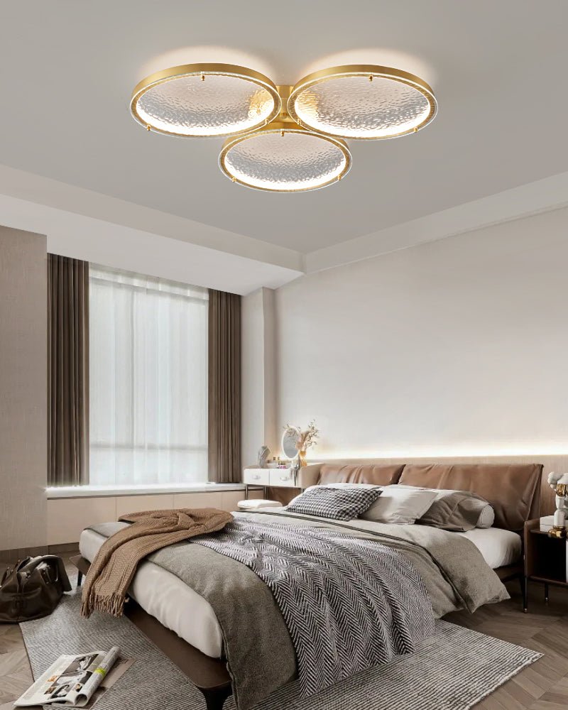 Three ring gold ceiling light above a bed with bedside lamps