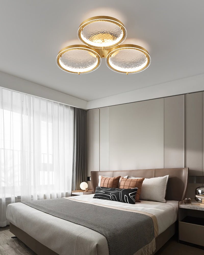 Three ring gold ceiling light lit in a bedroom at dusk