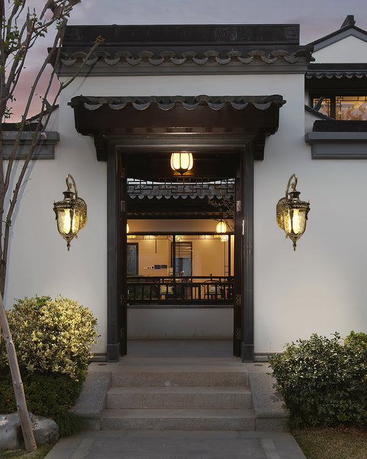 A pair of gold lanterns either side of a courtyard entrance door above stone steps